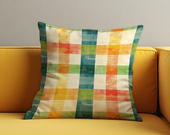 May include: Square throw pillow with a colorful plaid pattern in shades of orange, green, blue, and cream. The pillow is placed on a yellow sofa, creating a vibrant contrast. The pillow's design is reminiscent of a watercolor painting.