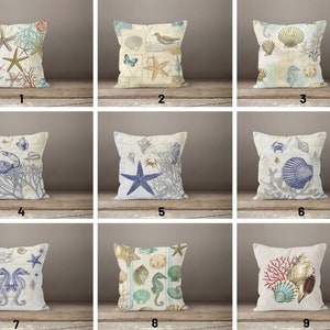 May include: Nine different throw pillow designs featuring a variety of coastal and nautical themes. Each pillow features a different combination of seashells, starfish, seahorses, crabs, coral, and other ocean-inspired elements. The pillows are all white with a light blue and beige colour scheme.