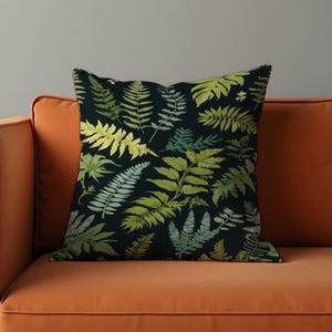 May include: A black cushion with a green fern pattern. The cushion is sitting on an orange sofa.