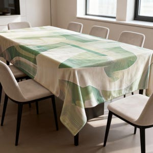 May include: A rectangular tablecloth with a geometric design in shades of green and white covers a dining table. The pattern features curved lines and shapes. The table is surrounded by beige chairs with black legs, creating a modern dining setting.