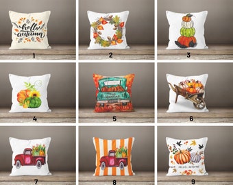 Puede incluir: Nueve diseños diferentes de almohadas decorativas con temas otoñales. Los diseños incluyen calabazas, hojas de otoño, un camión con calabazas, una corona y una carretilla con calabazas. Las almohadas son todas blancas con diseños de diferentes colores.
