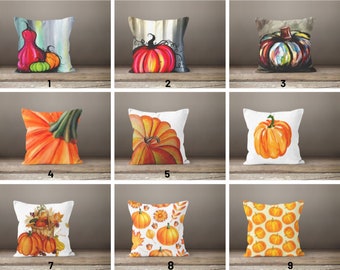 Puede incluir: Nueve diseños diferentes de almohadas decorativas con ilustraciones de calabazas. Las almohadas son blancas con una variedad de diseños de calabazas coloridos, incluyendo naranja, rojo, verde y amarillo.
