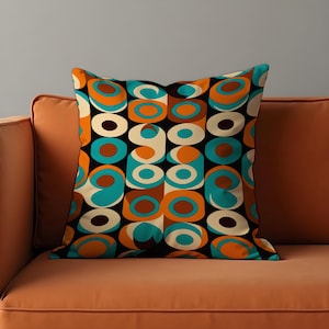 May include: Square cushion featuring a retro geometric design in orange, teal, brown, and cream on a black backdrop. The cushion is placed on an orange sofa.