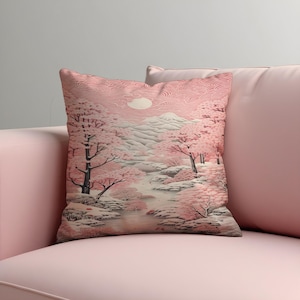 May include: A decorative cushion with a Japanese landscape design. The image shows a river, cherry blossom trees, and a mountain range in pink, white, and grey. The cushion has a textured surface and a soft appearance.