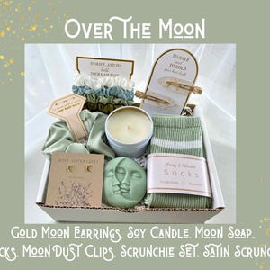 May include: A gift box with the text "Over The Moon" contains gold moon earrings, a soy candle, moon soap, socks, moon dust clips, a scrunchie set, and a satin scrunchie. The box includes hair accessories and a candle.