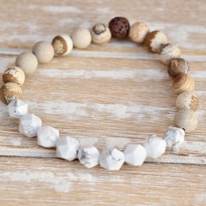 Op de afbeelding: Een bruin en witte edelsteen armband met een lava-kraal. De armband is gemaakt met ronde en gefacetteerde kralen.