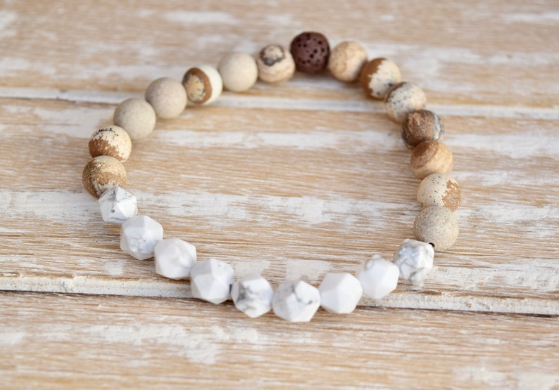 Op de afbeelding: Een bruin en witte edelsteen armband met een lava-kraal. De armband is gemaakt met ronde en gefacetteerde kralen.