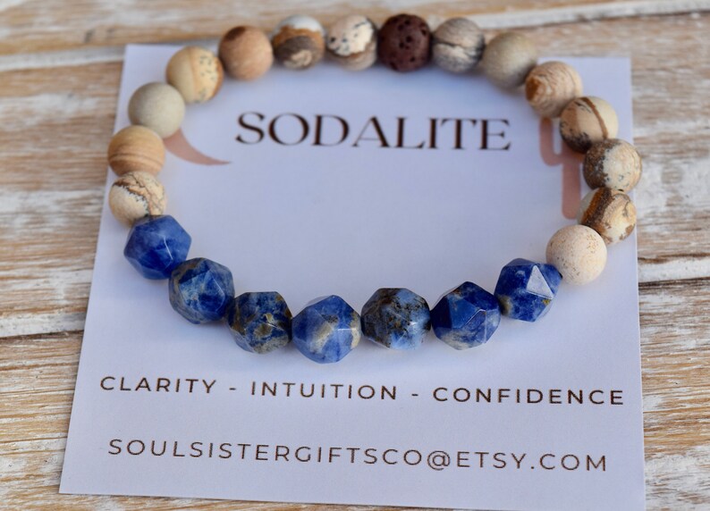 May include: A blue sodalite gemstone bracelet with brown and white jasper beads. The bracelet is on a white card with the text "Sodalite", "Clarity - Intuition - Confidence", and "Soulsistergiftsco@etsy.com".