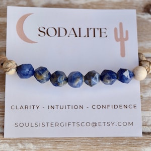 May include: A blue sodalite gemstone bracelet with brown and white speckled beads. The bracelet is on a white card with the words "Sodalite", "Clarity - Intuition - Confidence", and "Soulsistergiftsco@etsy.com".