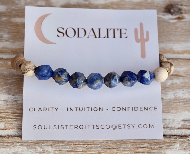 May include: A blue sodalite gemstone bracelet with brown and white speckled beads. The bracelet is on a white card with the words "Sodalite", "Clarity - Intuition - Confidence", and "Soulsistergiftsco@etsy.com".