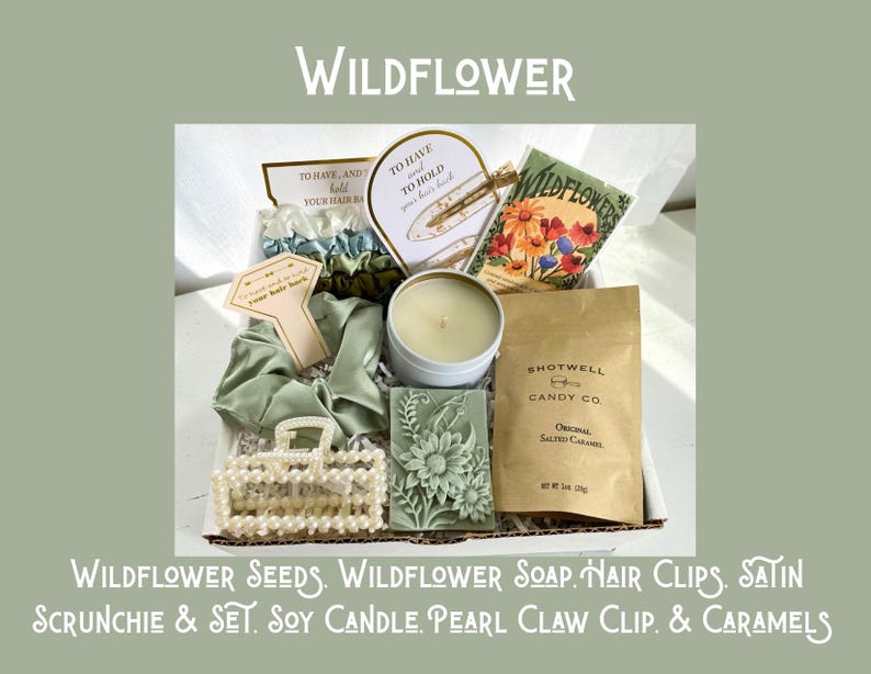 May include: A gift box with the word "WILDFLOWER" at the top. The box contains wildflower seeds, soap, hair clips, a satin scrunchie set, a soy candle, a pearl claw clip, and caramels. The box is filled with various items in shades of green and white.