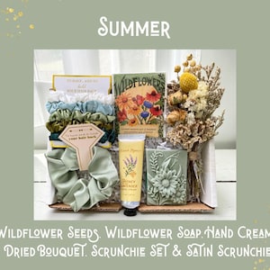May include: A gift box with the word "Summer" at the top. The box contains a scrunchie set, a satin scrunchie, wildflower seeds, a dried bouquet, wildflower soap, and honey lavender hand cream. The text "To have and to hold your hair back" is visible.