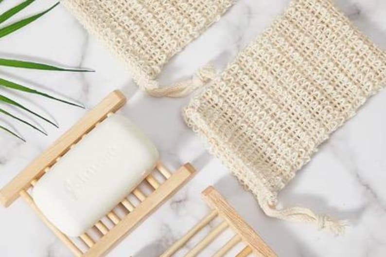 May include: Two white crocheted soap pouches with drawstrings and a white bar of soap in a wooden soap dish.