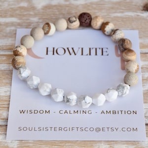 Op de afbeelding: Een witte howliet edelsteen armband met bruine en beige jasper kralen. De armband ligt op een witte kaart met de tekst "HOWLITE", "WISDOM - CALMING - AMBITION" en "SOULSISTERGIFTSCO@ETSY.COM".
