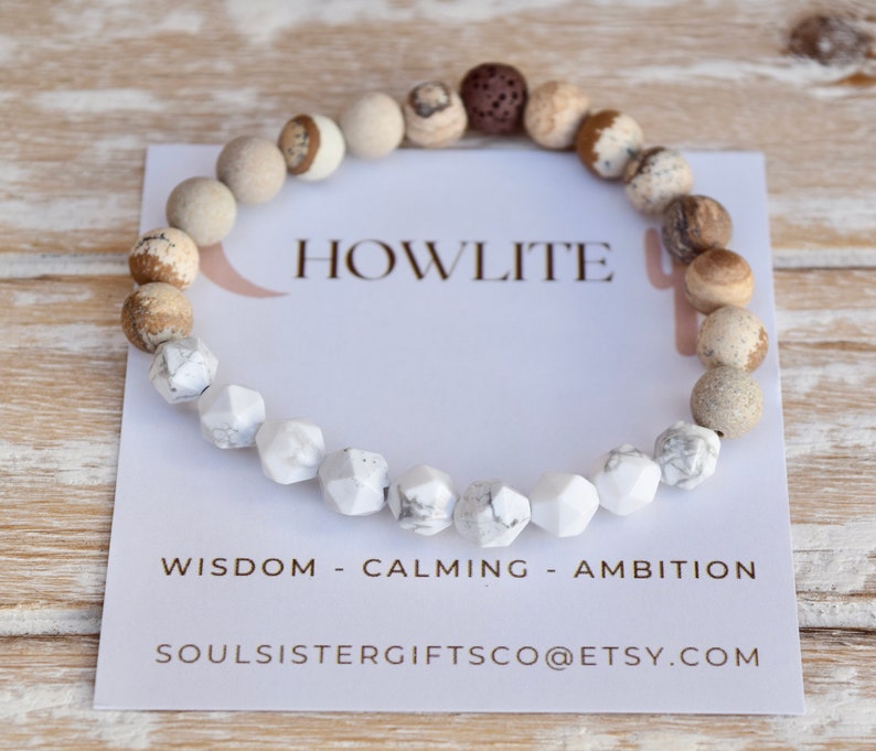 Op de afbeelding: Een witte howliet edelsteen armband met bruine en beige jasper kralen. De armband ligt op een witte kaart met de tekst "HOWLITE", "WISDOM - CALMING - AMBITION" en "SOULSISTERGIFTSCO@ETSY.COM".