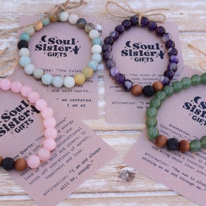 May include: Four bracelets with different colored stones and a lava bead. Each bracelet has a card with the name of the stone, its properties, and an affirmation. The cards are labeled "Soul Sister Gifts".