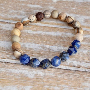 May include: A beaded bracelet with brown, white, and blue stones. The bracelet has a gradient of colors, starting with brown and white stones and transitioning to blue stones.