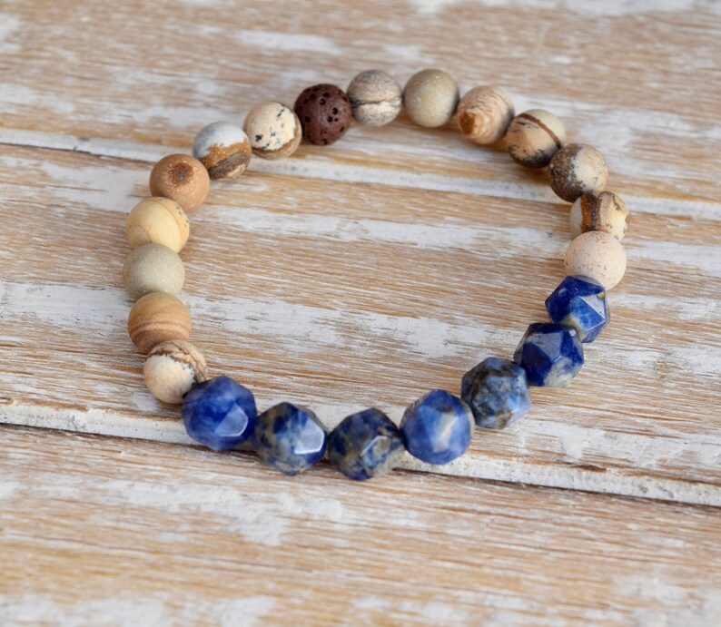 May include: A beaded bracelet with brown, white, and blue stones. The bracelet has a gradient of colors, starting with brown and white stones and transitioning to blue stones.