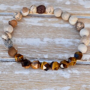 May include: A brown and white gemstone bracelet with a row of tiger's eye beads in the center.