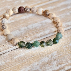May include: A bracelet made of light brown and grey stones with a row of dark green, faceted stones in the centre.