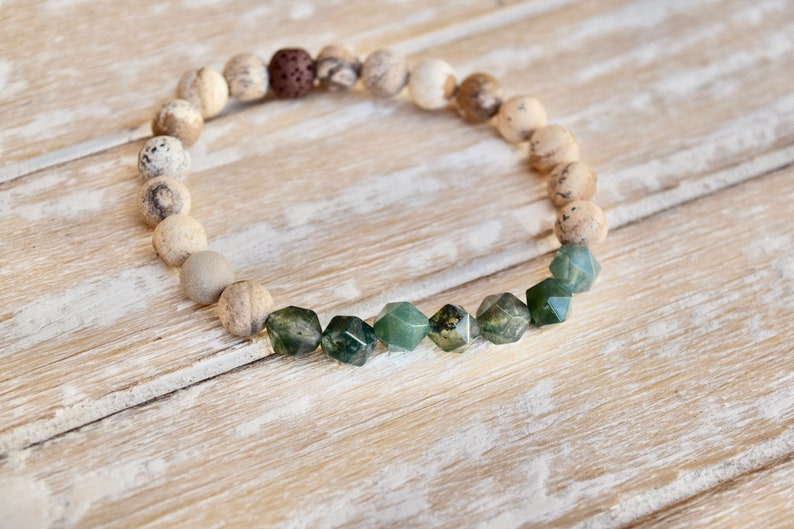 May include: A bracelet made of light brown and grey stones with a row of dark green, faceted stones in the centre.