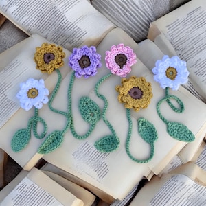May include: Five crocheted flower bookmarks with green leaves. The flowers are in shades of purple, pink, white, and yellow.