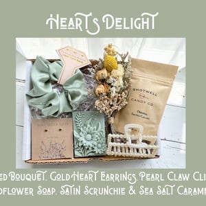 May include: A gift box with a variety of items, including a dried bouquet, gold heart earrings, a pearl claw clip, wildflower soap, a satin scrunchie, and sea salt caramels. The box is labeled "Heart's Delight."