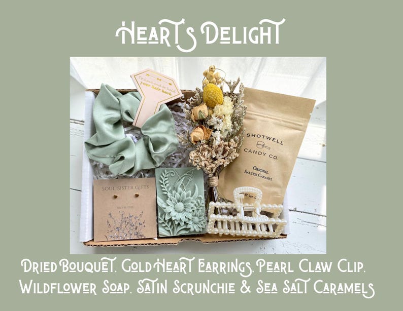 May include: A gift box with a variety of items, including a dried bouquet, gold heart earrings, a pearl claw clip, wildflower soap, a satin scrunchie, and sea salt caramels. The box is labeled "Heart's Delight."