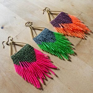 May include: Three pairs of handmade beaded earrings with a fringe design. Each pair features a different colour combination: pink and green, green and orange, and purple and orange. The earrings have gold-coloured ear wires and a rectangular top.