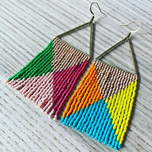 May include: A pair of triangle shaped earrings with colorful beaded fringe. The earrings are made with gold colored wire and feature pink, green, orange, yellow, and blue beads.