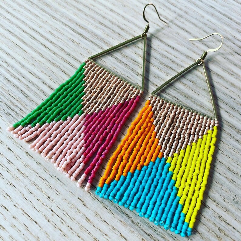 May include: A pair of triangle shaped earrings with colorful beaded fringe. The earrings are made with gold colored wire and feature pink, green, orange, yellow, and blue beads.