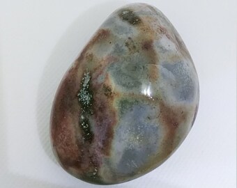 Può includere: Una pietra liscia di forma ovale con un motivo unico di colori marrone, grigio e bianco. La pietra ha una finitura lucida e un aspetto naturale e organico.