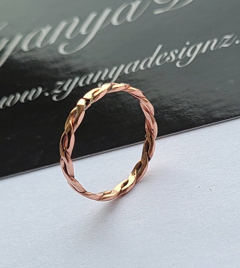 May include: A braided copper ring with a rose gold finish.