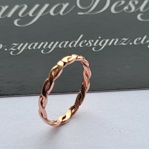 May include: A rose gold braided ring. The ring is made of a thin, twisted wire.