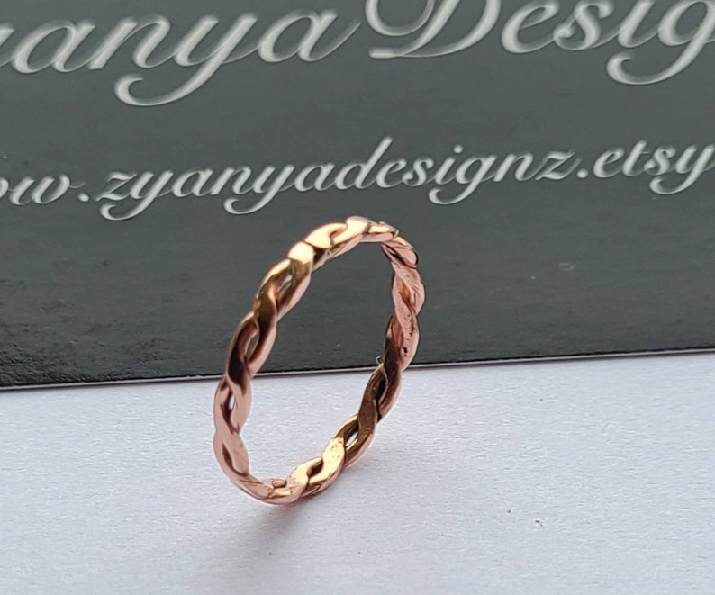 May include: A rose gold braided ring. The ring is made of a thin, twisted wire.