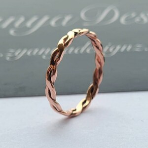May include: A rose gold braided ring. The ring is made of a thin, twisted band of metal.