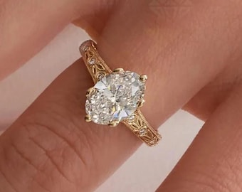 Può includere: Un anello d'oro con un diamante taglio ovale. L'anello presenta un design a filigrana dettagliato sulla fascia e intorno all'incastonatura del diamante. Il diamante brilla intensamente. L'anello è mostrato su un dito.