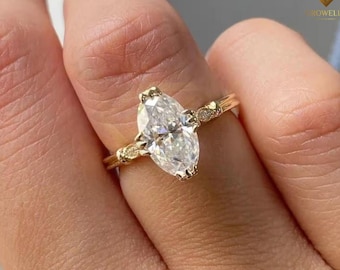 May include: A gold ring featuring a large marquise-cut clear gemstone as the center stone. The band is crafted from yellow gold and includes small, round accent stones embedded along the shoulders on both sides of the central marquise setting.