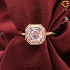May include: A rose gold ring featuring an octagonal-shaped center stone with a clear, faceted appearance. The setting has a milgrain edge detail around the stone and a thin, textured band. The word GROWELLO is printed at the bottom of the image.