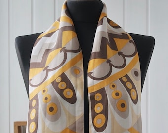 Può includere: Una sciarpa di seta con motivi geometrici, di colore marrone, bianco e giallo. La sciarpa è esposta su un manichino nero.