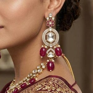 May include: A woman wearing a set of ornate jewelry, including earrings, a necklace, and a headpiece. The earrings feature a circular design with a central clear stone and ruby-colored accents. The necklace and headpiece also have ruby-colored stones.