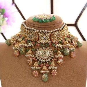 Pode incluir: Um conjunto de colar e brincos de ouro com contas verdes e rosa, pérolas e desenhos florais intrincados. O colar tem um estilo de gargantilha com um pingente que cai. Os brincos combinam e têm um design semelhante.