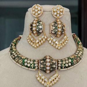 May include: A gold-toned jewelry set featuring a necklace and matching earrings. The necklace and earrings have a green enamel design with white floral accents and clear gemstones. The earrings are a drop style, and the necklace is a choker.