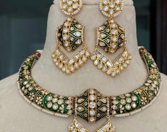 May include: A gold-toned jewelry set featuring a necklace and matching earrings. The necklace and earrings have a green enamel design with white floral accents and clear gemstones. The earrings are a drop style, and the necklace is a choker.