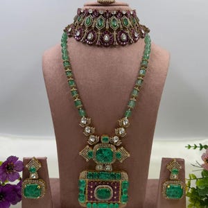 May include: A jewelry set featuring a choker necklace, a long pendant necklace, and matching earrings. The pieces are crafted with gold-tone metal, green rectangular stones, and deep pink circular stones, accented with small clear white crystals.