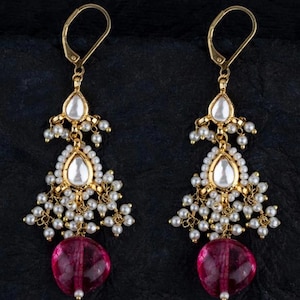 Peut inclure: Une paire de boucles d'oreilles en or avec un design en forme de larme. Les boucles d'oreilles présentent des perles blanches, des pierres claires et une pierre précieuse rose en bas.