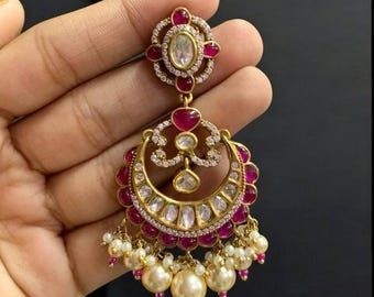 May include: Gold-toned earring with a crescent moon design, adorned with red and clear gemstones. The earring features a cluster of dangling pearls at the bottom. The top has a floral design with a large oval gemstone.