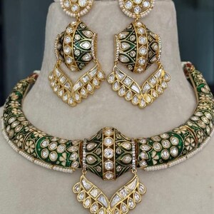 May include: A gold-toned jewelry set featuring a necklace and matching earrings. The set has a green and white floral design with clear, sparkling accents. The earrings and necklace have a drop design.