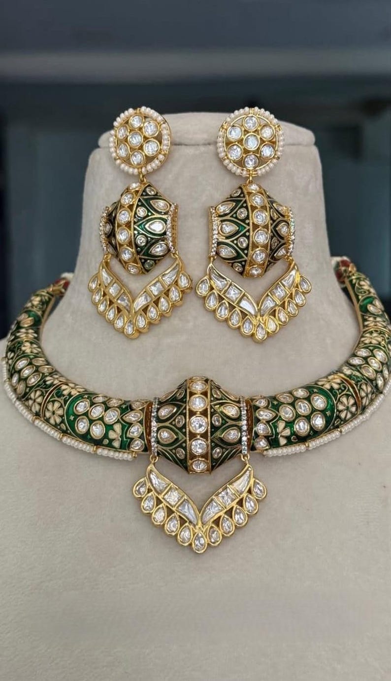 May include: A gold-toned jewelry set featuring a necklace and matching earrings. The set has a green and white floral design with clear, sparkling accents. The earrings and necklace have a drop design.