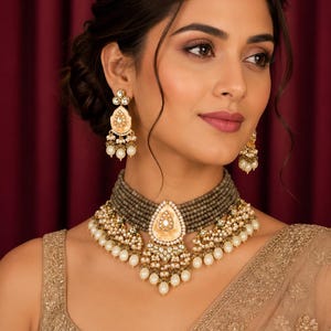 Peut inclure: Un collier ras-de-cou composé de multiples rangs de perles grises avec un pendentif central en forme de goutte en émail crème, métal doré et perles blanches, accompagné de boucles d'oreilles assorties en forme de goutte avec perles.